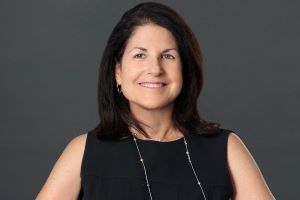 Headshot of Dr. Donna Shelley. She is wearing a black top and she is standing in front of a dark grey background.