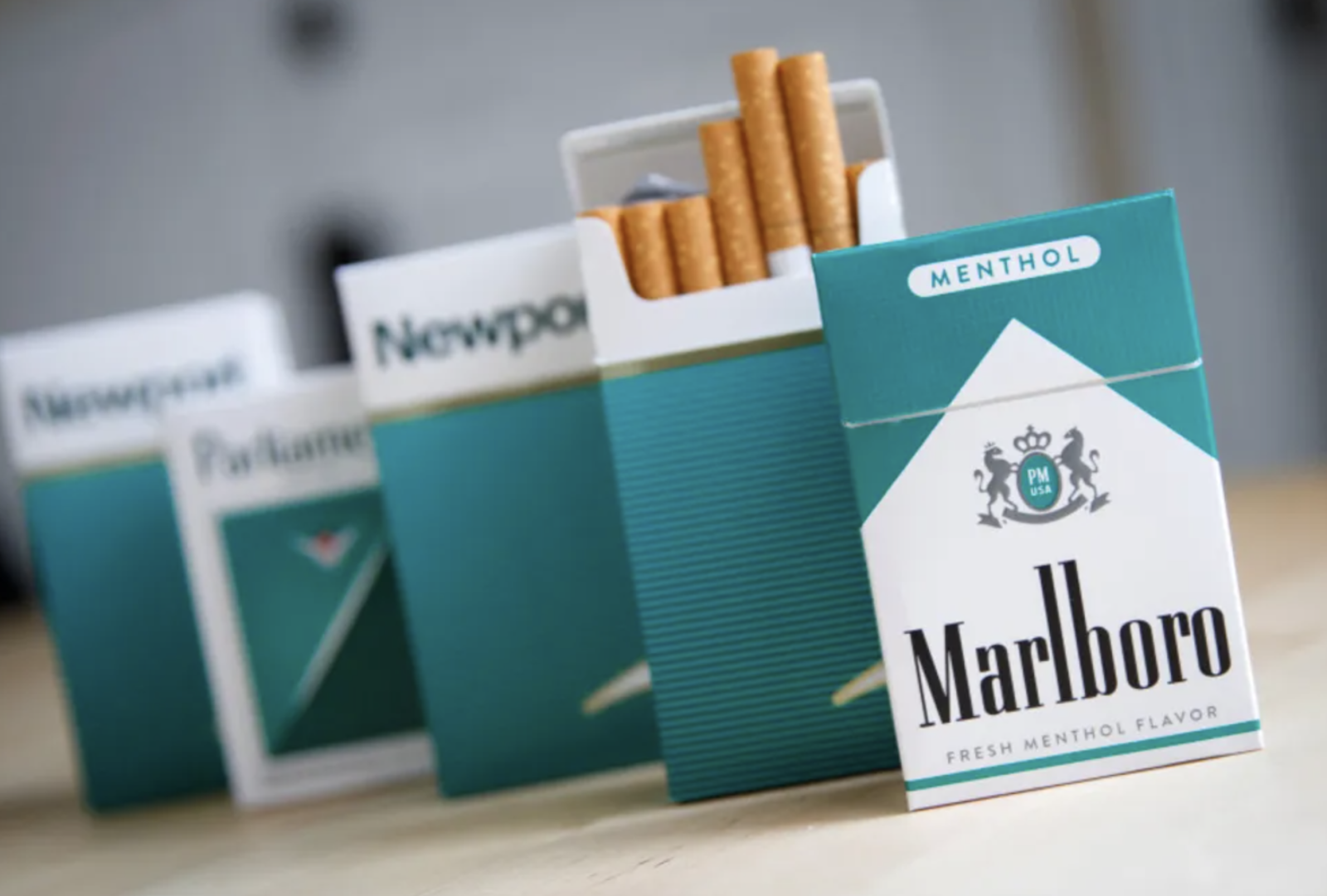 A photo of different brands of menthol cigarettes stacked on a wooden table.